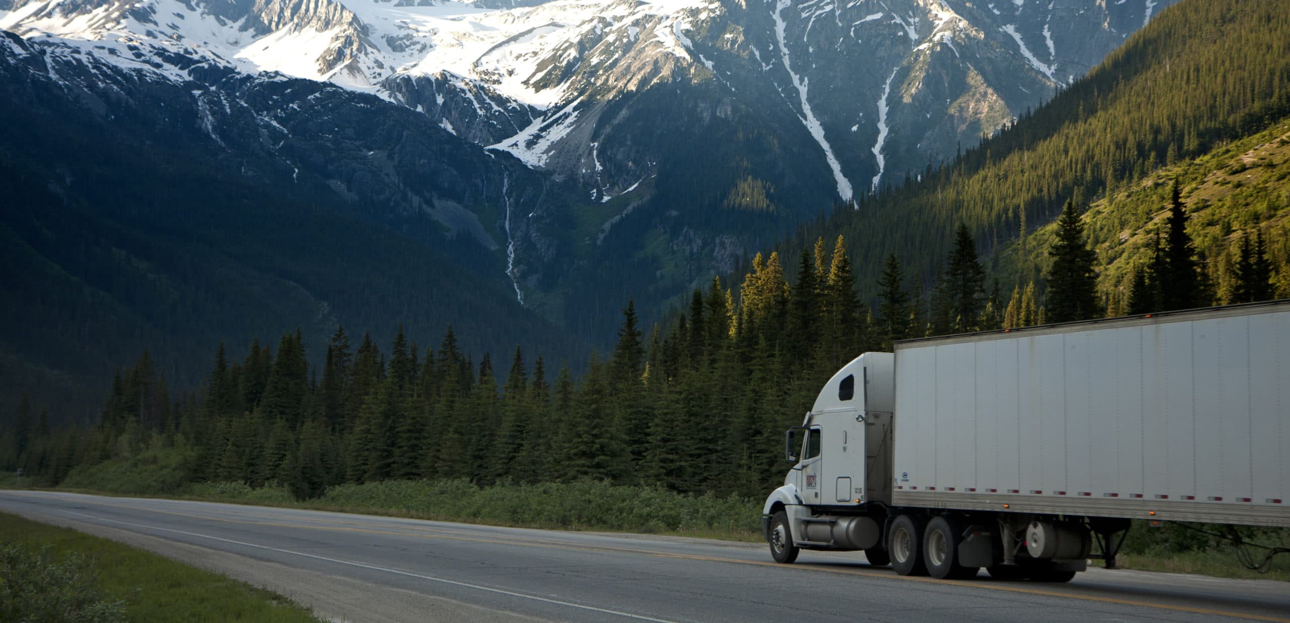 White HGV travelling along a mountain highway representing Plexus Freight's road freight services