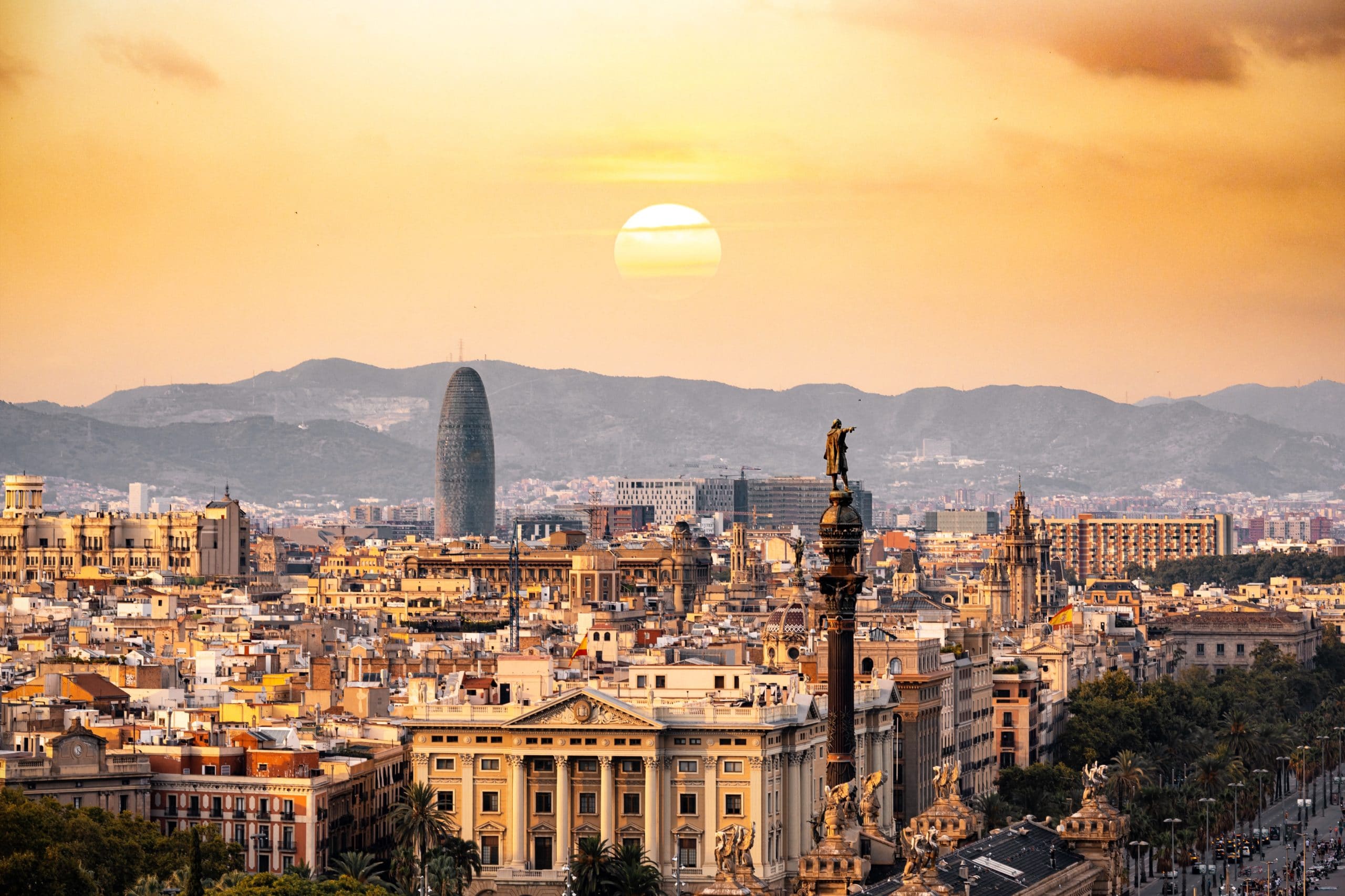 Barcelona skyline at sunset with the Columbus Monument and Torre Agbar tower against a golden sky