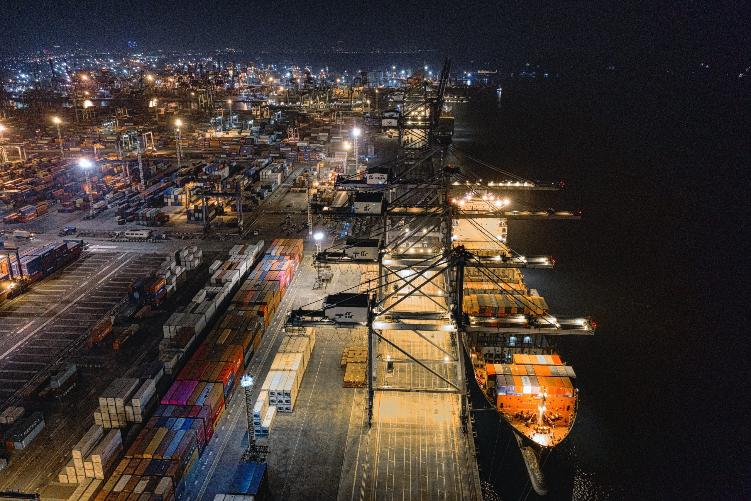 Aerial night view of container port with ship and cranes representing Plexus Freight's sea freight operations