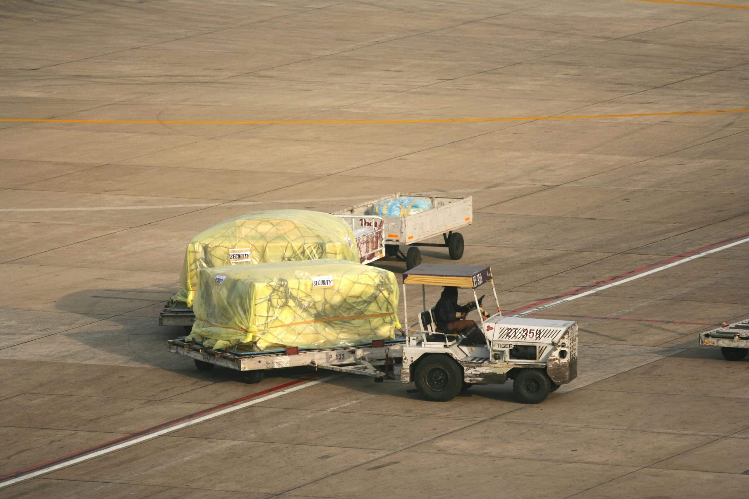 Ground vehicle towing netted air freight pallets across an airport apron