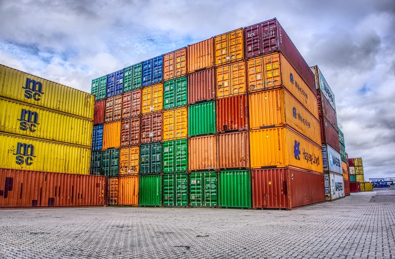 Large block of multicoloured shipping containers stacked high in a container yard under a cloudy sky